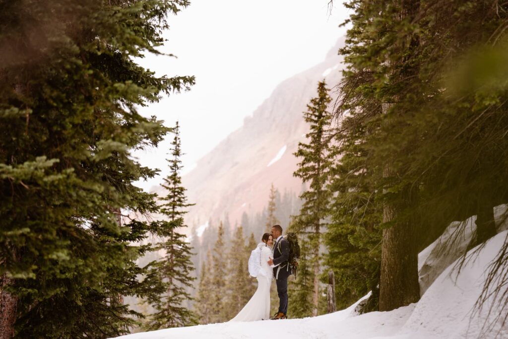 Couple hiking in their wedding attire in the snowy red mountains of Ouray, Colorado