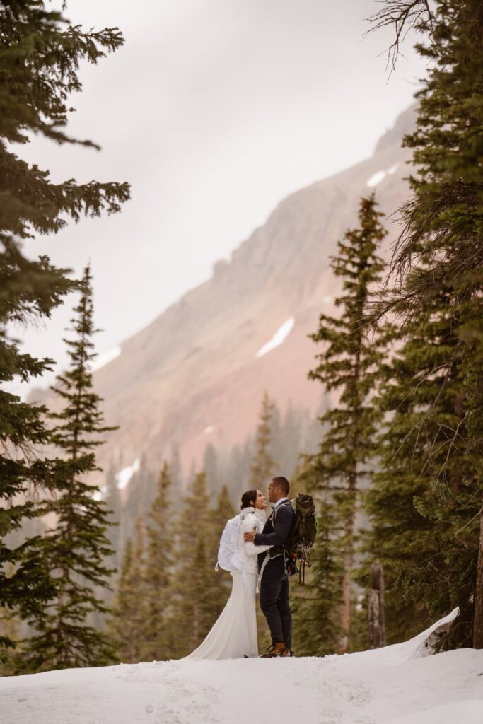 Bride and groom kissing in the snow with red mountains in the distance