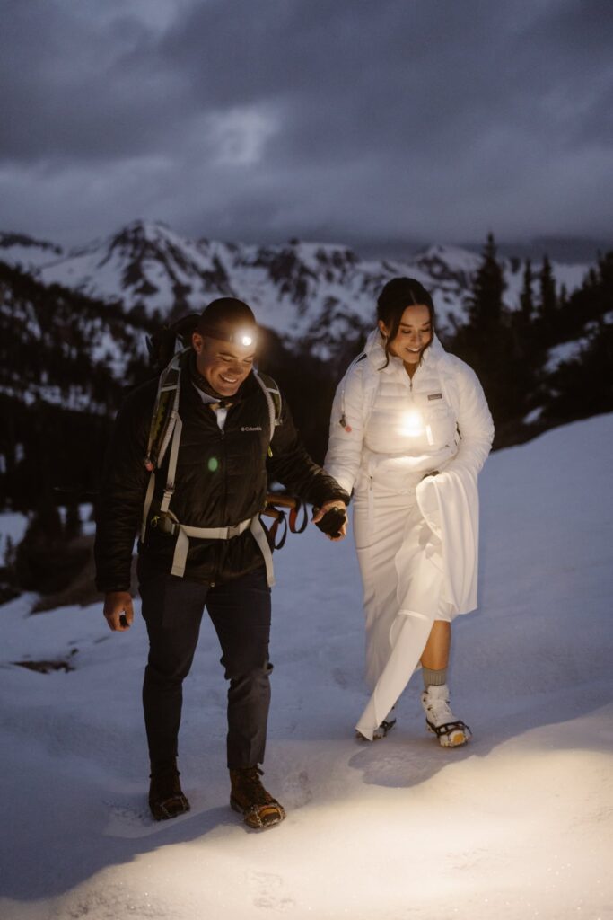 Bride and groom hiking up in the snow under a night sky with headlamps