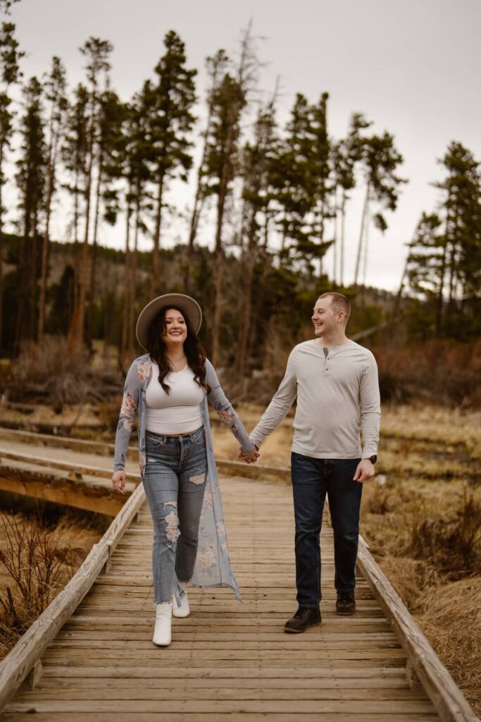Couple walking down a wood boardwalk in the mountains during their engagement session